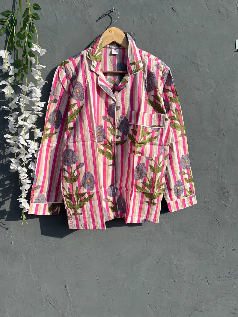 May include: A pink and white striped shirt with a floral print. The shirt has a button-up collar and long sleeves.