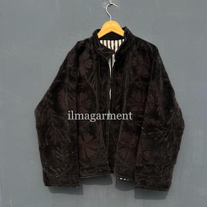 Puede incluir: Chaqueta de terciopelo negro con bordado floral, colgada de una percha de madera. La chaqueta tiene un forro a rayas y el texto "ilmagarment" es visible en la parte delantera. La chaqueta es de color oscuro y parece estar hecha de un material suave.