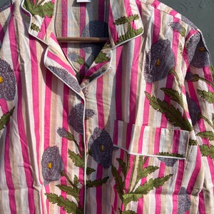 May include: A pink and white striped shirt with a floral print. The shirt has a button-up front and a collar. The size "M" is visible on the tag.