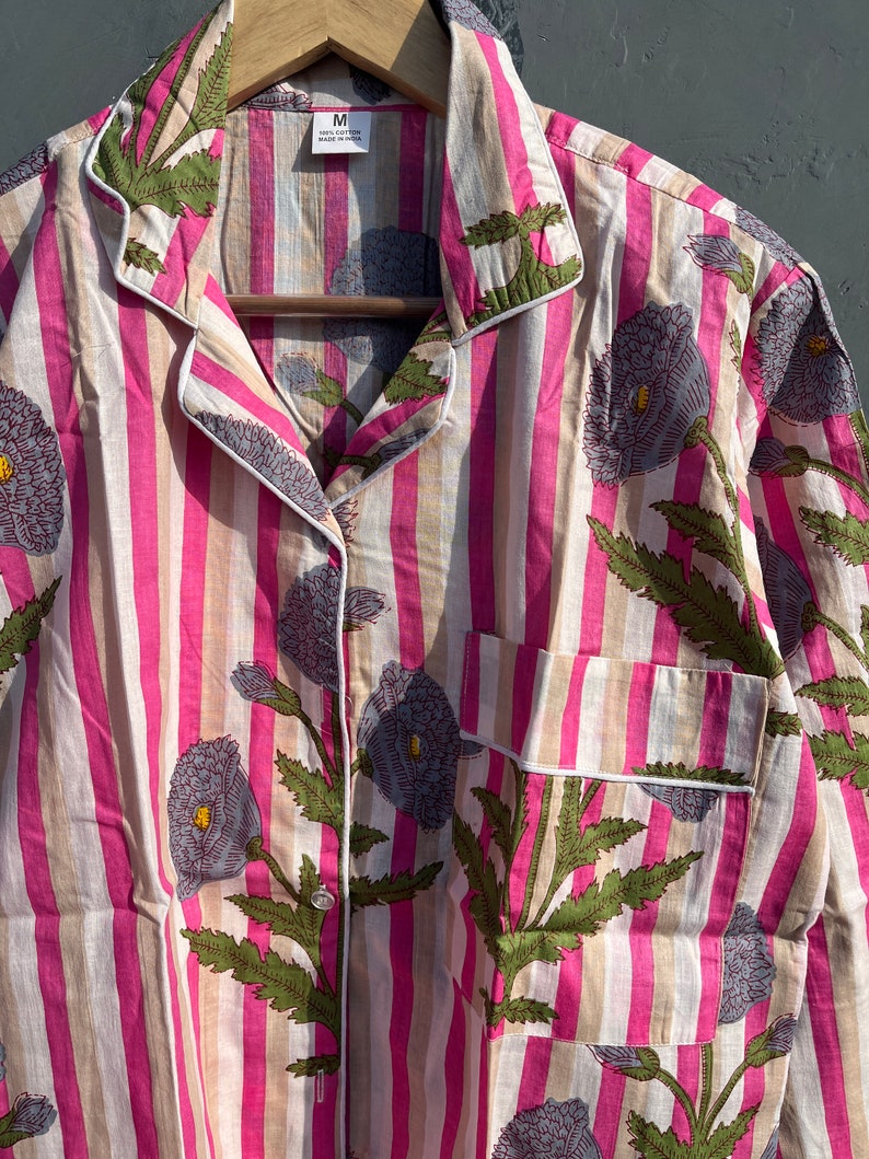 May include: A pink and white striped shirt with a floral print. The shirt has a button-up front and a collar. The size "M" is visible on the tag.