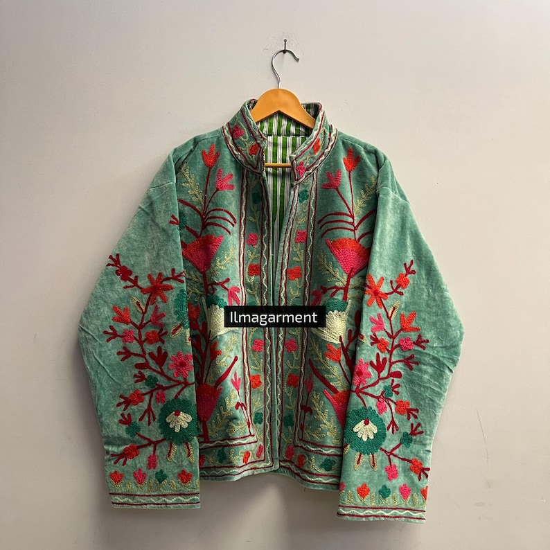 May include: A light green velvet jacket with intricate floral embroidery in shades of pink, red, and green. The jacket features a high collar and is lined with a striped fabric. The text "llmagarment" is visible on the front.