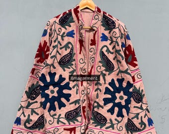 May include: A light pink jacket with intricate floral embroidery in shades of red, blue, green, and navy. The jacket is hanging on a wooden hanger. The text "Ilmagarment" is visible on the jacket.