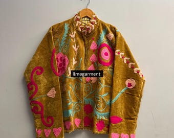 May include: Mustard-colored jacket with floral embroidery in pink, teal, and light pink. The jacket features a high collar and is hanging on a wooden hanger. The text "llmagarment" is visible on the jacket.