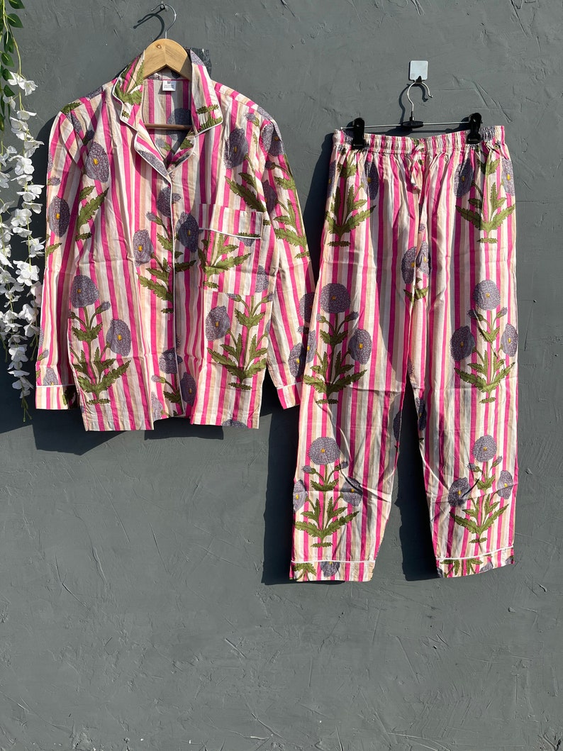 May include: Pink and white striped pajama set with a floral print. The top has long sleeves and a button-up front. The pants have an elastic waistband.