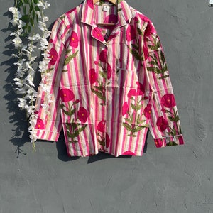 Puede incluir: Una camisa de manga larga a rayas rosa y blancas con estampado floral. La camisa tiene cuello y cierre de botones.