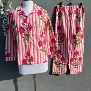 Puede incluir: Un conjunto de pijama a rayas rosa y blanco con estampado floral. La parte superior tiene mangas largas y un cierre de botones en la parte delantera. Los pantalones tienen una cintura el&aacute;stica.