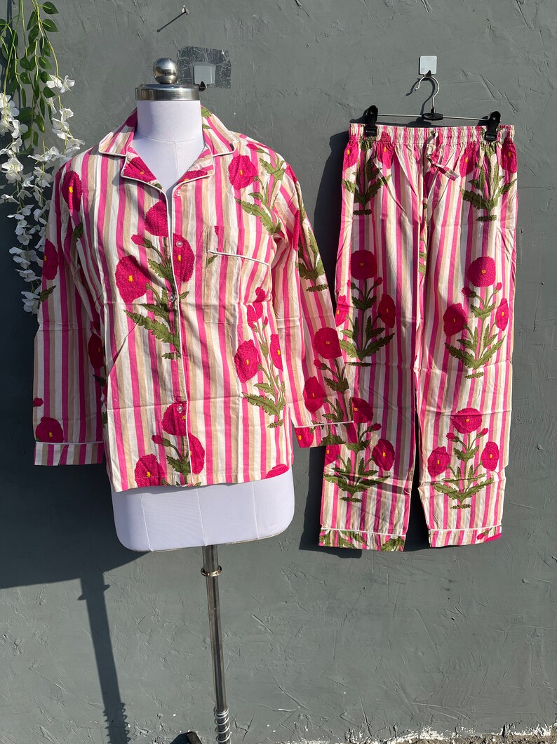Puede incluir: Un conjunto de pijama a rayas rosa y blanco con estampado floral. La parte superior tiene mangas largas y un cierre de botones en la parte delantera. Los pantalones tienen una cintura el&aacute;stica.