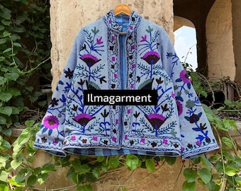 May include: A blue jacket with intricate floral embroidery in purple, blue, and green. The jacket features a high collar and is hanging on a wooden hanger. The text "llmagarment" is displayed on the front of the jacket.