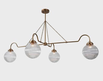 May include: A brass-toned, multi-light chandelier with four clear, ribbed glass globe shades. The fixture is suspended from the ceiling by a central rod and chains, with curved arms extending to hold the shades. The design is modern and elegant.