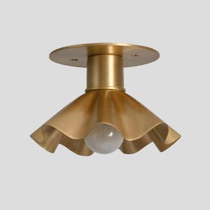May include: A brass-colored ceiling light fixture with a ruffled shade and a round base. The light has a single bulb and a cylindrical stem connecting the shade to the base. The fixture is designed for indoor use.