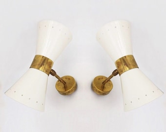 Puede incluir: Un par de apliques de pared blancas y de latón con una pantalla en forma de cono. Las pantallas tienen un patrón de puntos y una banda de latón en el medio.