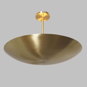 May include: A contemporary ceiling light in a brass finish. The light features a large, shallow, bowl-shaped shade suspended from a central rod and a circular ceiling mount. The fixture has a minimalist design and a warm, metallic finish.