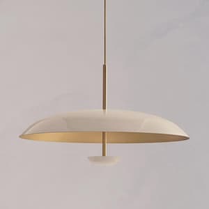 May include: Cream-coloured pendant light with a gold interior and a brass-coloured stem. The light fixture has a rounded, saucer-like shade and a small, inverted bowl-shaped element at the bottom. The light hangs from a thin wire.