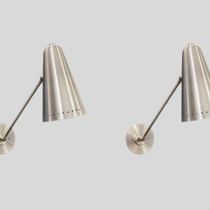 Op de afbeelding: Een paar zilveren wandlampen met verstelbare armen en kegelvormige lampenkappen. De lampenkappen hebben een geperforeerd patroon.