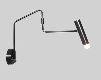 May include: A black, adjustable wall-mounted lamp with a cylindrical head and a single light bulb. The lamp has a pivoting arm and a circular base, designed for directional lighting. The fixture is made of metal.