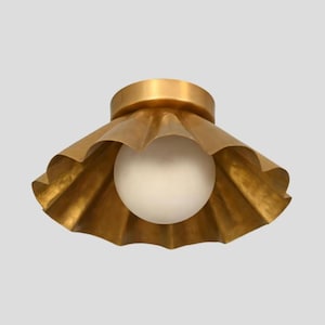 May include: A gold-colored ceiling light fixture with a scalloped shade and a round, white light bulb. The fixture has a circular base and a textured, ruffled design around the bulb. The light is designed to be mounted on a ceiling.