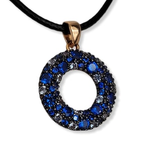 May include: A gold pendant necklace with a round, open circle design. The circle is covered in small blue and white gemstones.