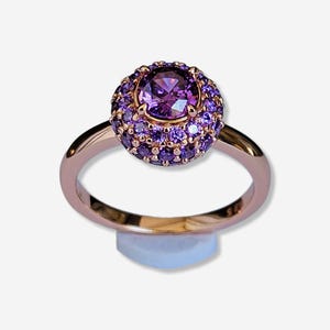 Könnte beinhalten: Ein Ring aus Roségold mit einem großen violetten Edelstein, der von kleineren violetten Edelsteinen umgeben ist.