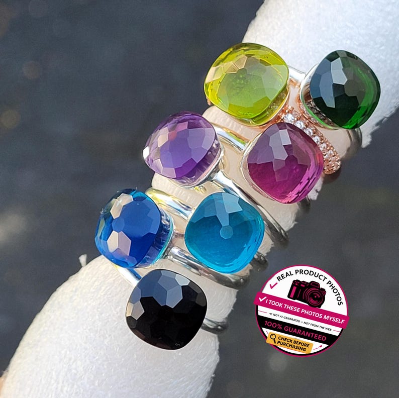 Puede incluir: Una colecci&oacute;n de anillos con piedras preciosas en varios colores, incluyendo morado, azul, verde y negro. Los anillos tienen una gema de corte cuadrado engastada en una banda plateada. La imagen tambi&eacute;n incluye un anillo con peque&ntilde;os diamantes y una pegatina que dice "REAL PRODUCT PHOTOS".