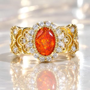 May include: A gold ring featuring a central oval-cut orange fire opal surrounded by a halo of small round white diamonds. The band is crafted with an intricate openwork filigree pattern that extends along the sides, also accented with small diamonds.