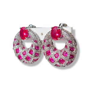 Op de afbeelding: Een paar zilveren oorringen met een roze robijn in het midden van elke ring. De ringen zijn bedekt met kleine roze en witte steentjes.