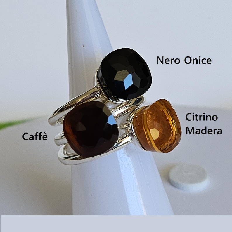 Puede incluir: Tres anillos con engastes de piedras preciosas facetadas en negro, marr&oacute;n y &aacute;mbar. Los anillos tienen una banda plateada. El texto de la imagen dice "Nero Onice", "Citrine Madera" y "Caff&egrave;".