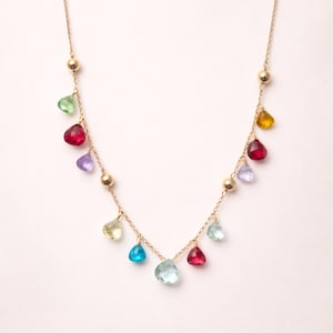 Peut inclure: Un collier à chaîne dorée orné d'une série de petites pierres précieuses en forme de goutte d'eau multicolores et de perles dorées lisses espacées le long de la chaîne. Les pierres incluent des nuances de rouge, bleu, vert, jaune et violet.