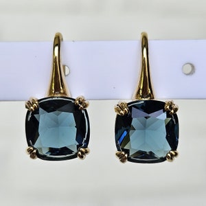Peut inclure: Une paire de boucles d'oreilles en or avec des pierres précieuses carrées bleu foncé. Les boucles d'oreilles ont un design simple avec une petite boucle en or en haut.