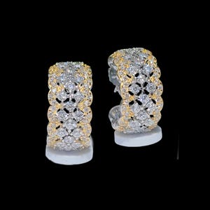 May include: A pair of hoop earrings with a two-tone design. The earrings feature a gold-colored band on the top and bottom, with a silver-colored band in the middle. The silver band is encrusted with small, clear gemstones.