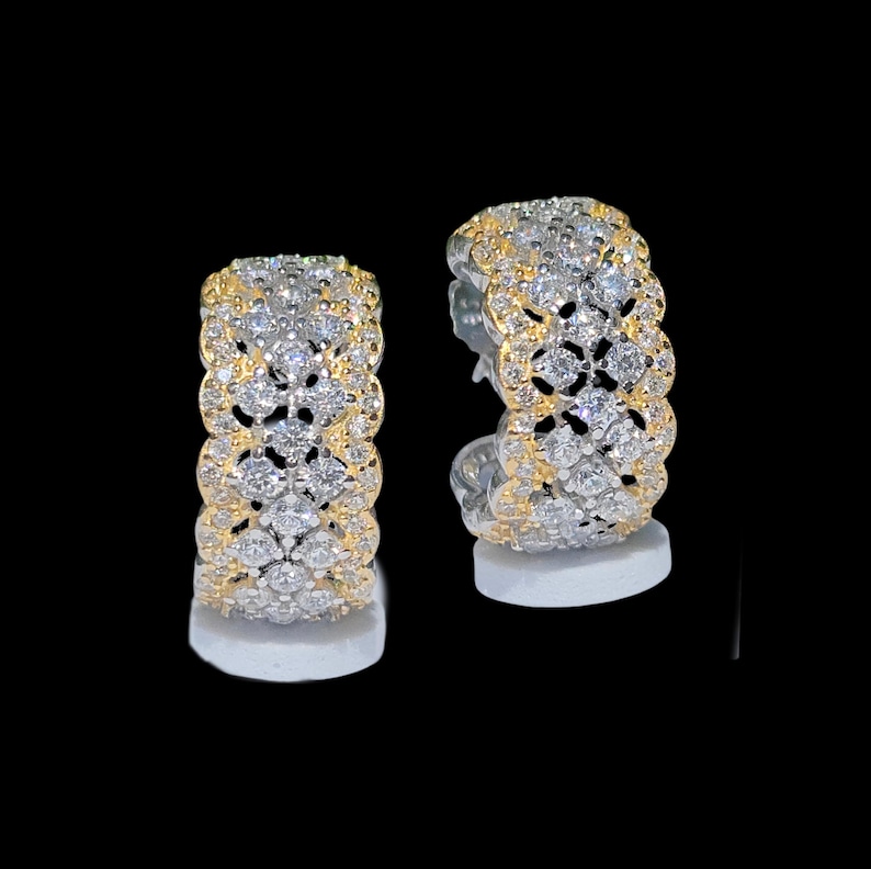 May include: A pair of hoop earrings with a two-tone design. The earrings feature a gold-colored band on the top and bottom, with a silver-colored band in the middle. The silver band is encrusted with small, clear gemstones.