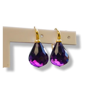 Könnte beinhalten: Ein Paar goldene Ohrringe mit violetten tropfenförmigen Kristallen.