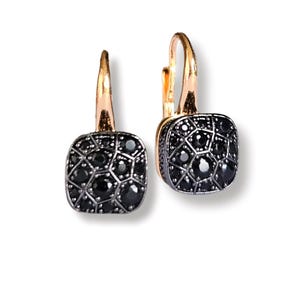 Puede incluir: Un par de pendientes cuadrados con ganchos dorados y bases plateadas. Cada cuadrado está adornado con piedras preciosas negras. Los pendientes se muestran sobre un fondo blanco.