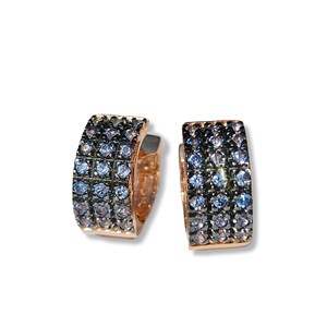 May include: A pair of rose gold hoop earrings. Each earring is encrusted with small, light blue and dark blue gemstones. The earrings have a rectangular shape and a hinged closure.