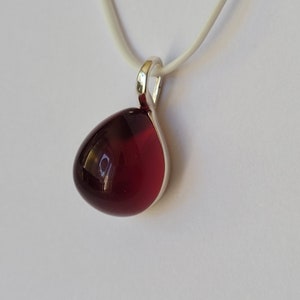 Op de afbeelding: Een zilveren hanger met een traanvormige rode glazen steen.