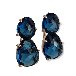 May include: A pair of gold tone earrings with two teardrop shaped blue gemstones.