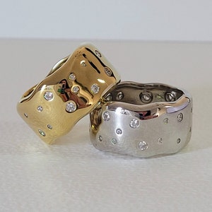 May include: Two rings with a wavy design, one is gold and the other is silver. Both rings are set with small diamonds.