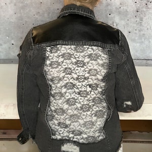May include: A black denim jacket with a black leather panel on the back and a white lace panel underneath.