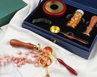 May include: A blue velvet box with a wooden base, a gold metal spoon, a wooden handle stamp, and a small glass jar filled with wax beads. The box also contains a small gold metal bowl with a red interior.