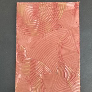 Peut inclure: Gros plan sur une surface texturée de couleur rouge-brun avec un motif de cercles concentriques. Les cercles sont en relief et ont un léger éclat.