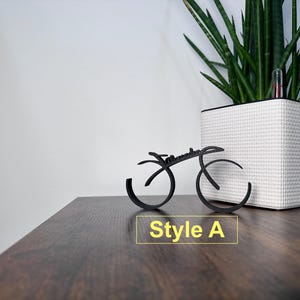 May include: A black metal bicycle sculpture with the word "remarkable" written on it. The sculpture is sitting on a wooden surface. The text "Style A" is written below the sculpture.