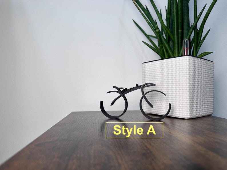 May include: A black metal bicycle sculpture with the word "remarkable" written on it. The sculpture is sitting on a wooden surface. The text "Style A" is written below the sculpture.