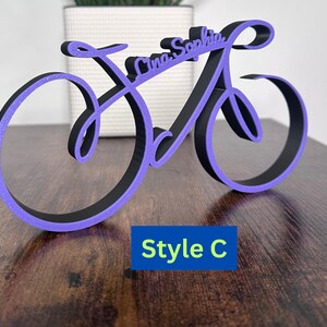 May include: Purple and black wooden bicycle-shaped sign with the names "Lina Sophia" written in a cursive font. The sign is labeled "Style C".