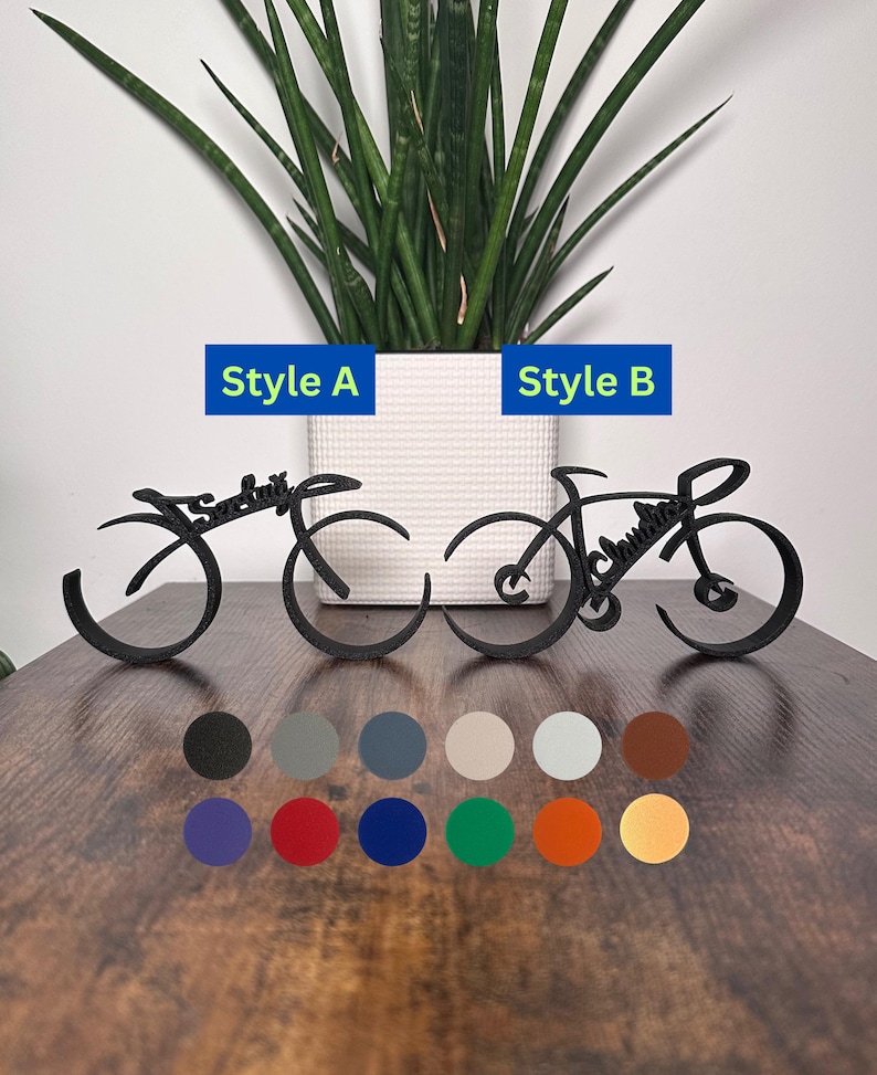May include: Two black metal bike sculptures, one in a simple design and the other with more detail, with the words "Sarah" and "Joshua" incorporated into the design. The sculptures are on a wooden surface with a variety of color options displayed below.