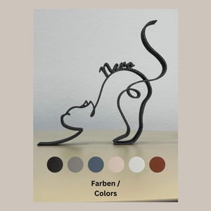 Könnte beinhalten: Eine schwarze Metallkatzenskulptur mit dem Wort "Meow" in Kursivschrift auf dem Rücken. Die Skulptur steht auf einer weißen Oberfläche mit einer Reihe von Farbmustern darunter.