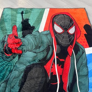 May include: A colorful throw blanket featuring a cartoon illustration of Spider-Man in a red and black suit with a green and blue background.