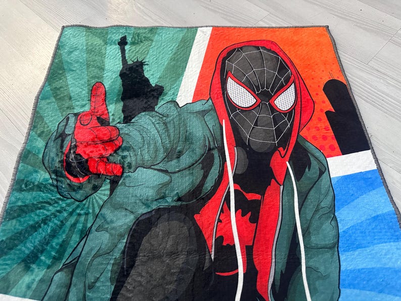 May include: A colorful throw blanket featuring a cartoon illustration of Spider-Man in a red and black suit with a green and blue background.
