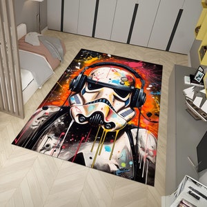 Puede incluir: Una alfombra colorida con un casco blanco de Stormtrooper con auriculares y salpicaduras de pintura. El fondo es de color naranja y amarillo vibrante con salpicaduras de azul, verde y rojo.