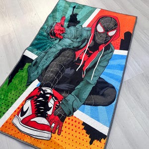 May include: A colorful rug featuring a cartoon illustration of Spider-Man wearing a red and black suit and red and white sneakers. The rug has a comic book style design with green, blue, orange, and yellow colors.