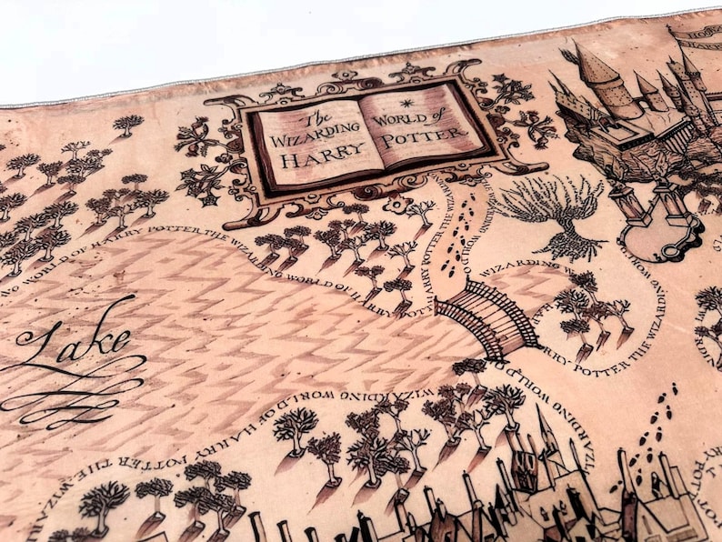 May include: A detailed map with the text "The Wizarding World of Harry Potter" in a decorative frame. The map features illustrations of a castle, trees, a bridge, and the word "Lake". The map is in shades of brown and tan.