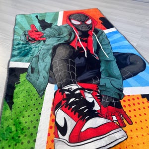 May include: A colorful rug featuring a cartoon superhero wearing a red and black suit and red and black sneakers. The rug has a comic book style design with red, blue, green, yellow, and white colors.